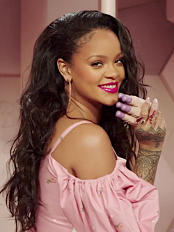 Rihanna sorrindo, segurando produtos da marca Fenty